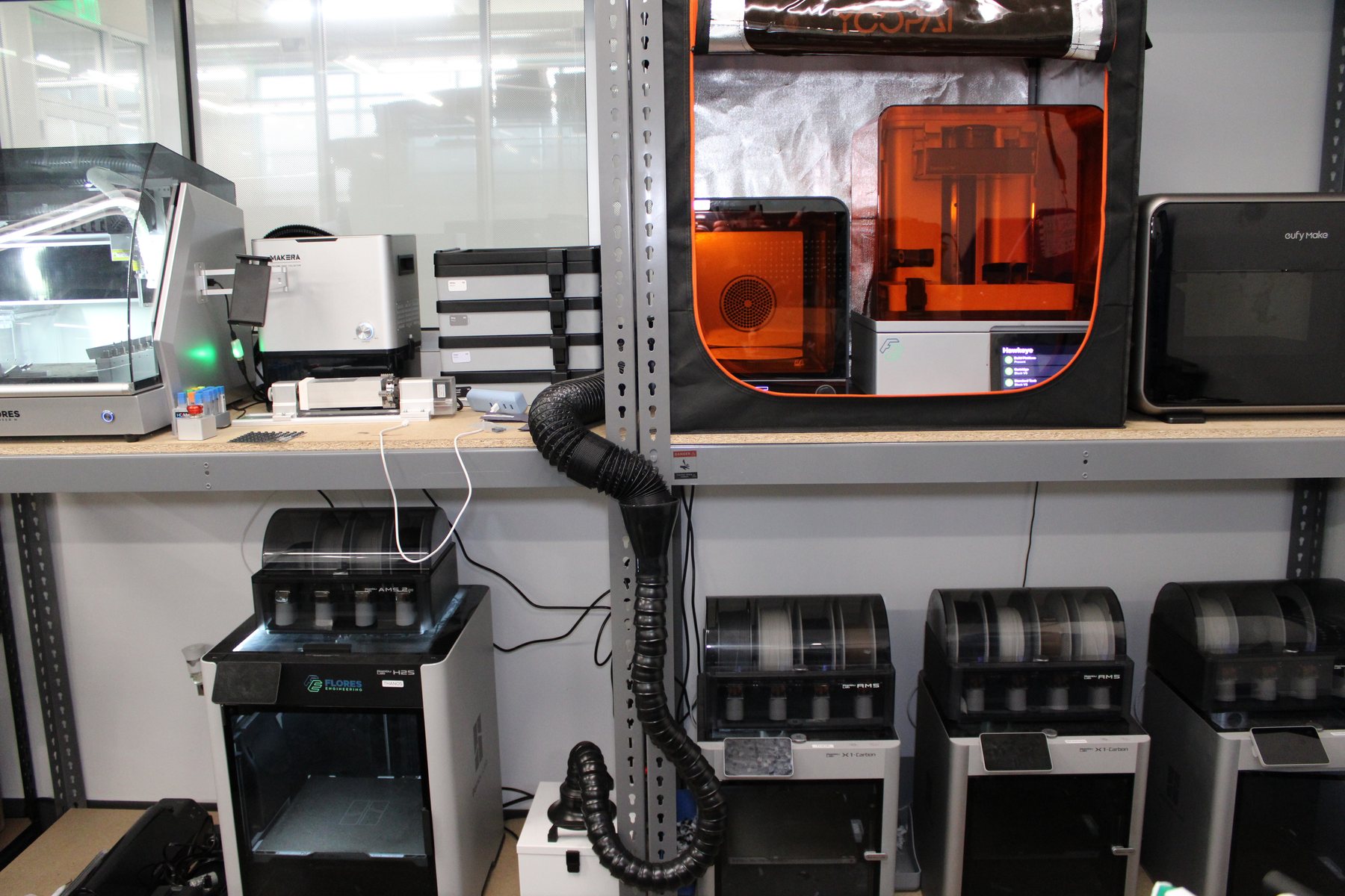 Prototyping wall in the Flores Engineering lab in Kearny, NJ, with SLA and FDM printers, a laser cutter and a desktop CNC